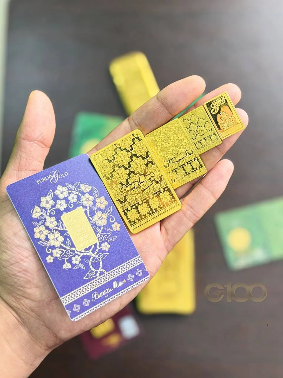 Tangan memegang beberapa kepingan gold bar Public Gold bersama kad gold certificate sebagai simpanan emas fizikal
